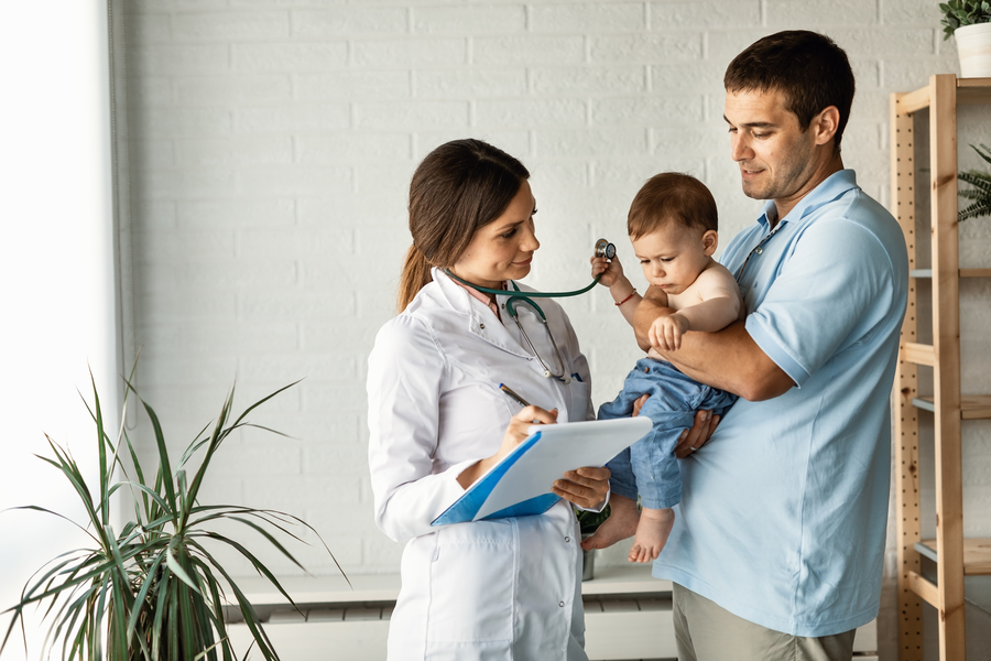Center pai adulto medio segurando seu filho pequeno e se comunicando com medica que esta tomando notas na area de transferencia